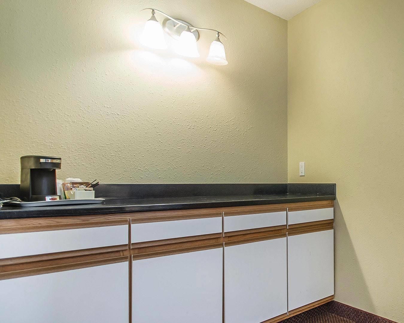 Un baño con lavabo, cafetera y una lámpara de pared.