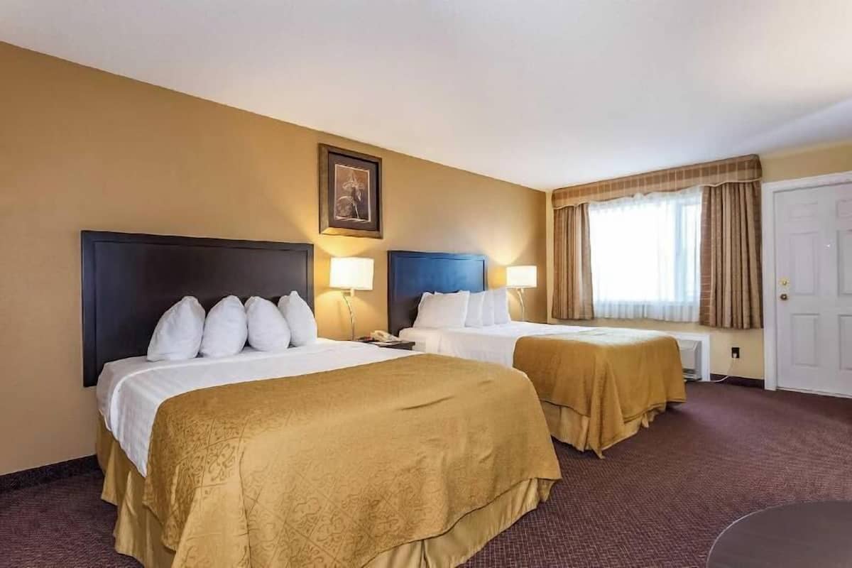 Habitación de hotel con dos camas, un ventanal con cortinas, una puerta y un cuadro en la pared.