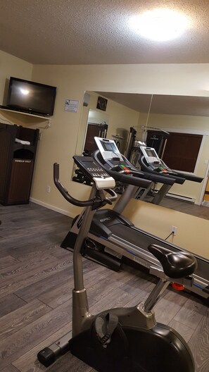 Une salle de sport à domicile équipée d’un tapis de course, d’un vélo d’exercice et d’un téléviseur fixé au mur.