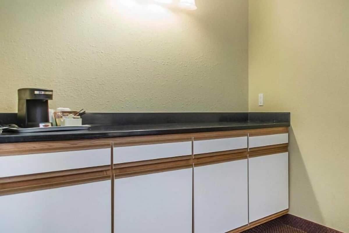 Un baño con encimera, cafetera e iluminación en la pared.