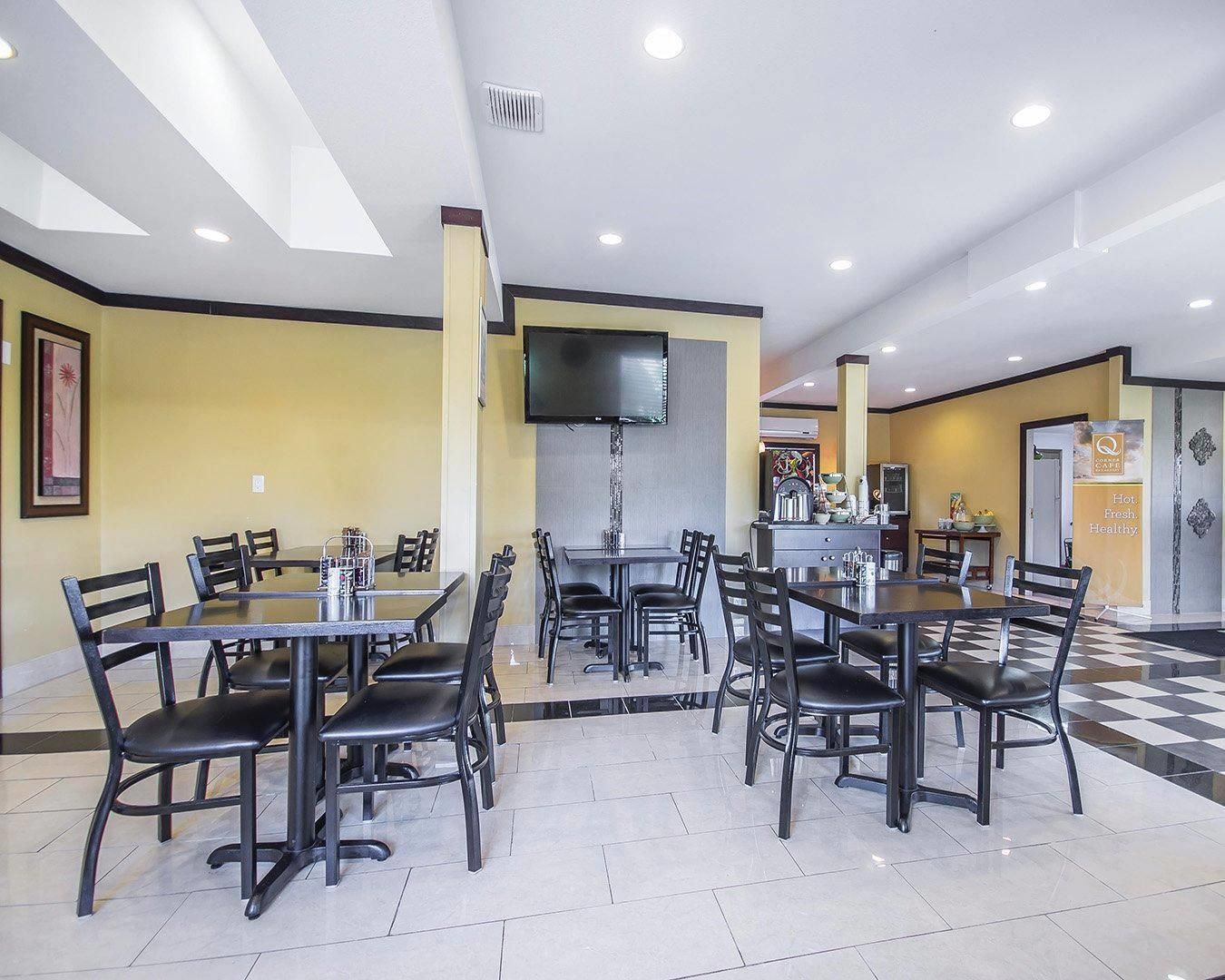 Un restaurante con varias mesas y sillas, un televisor de pantalla plana en la pared y un suelo con estampado de cuadros.