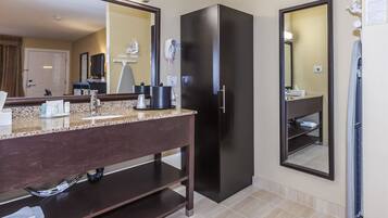 A modern bathroom with a granite countertop, dark cabinetry, a black refrigerator, and a large mirror.