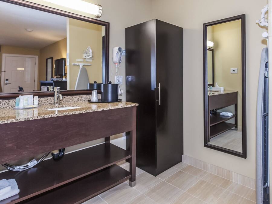 A modern bathroom with a granite countertop, dark cabinetry, a black refrigerator, and a large mirror.