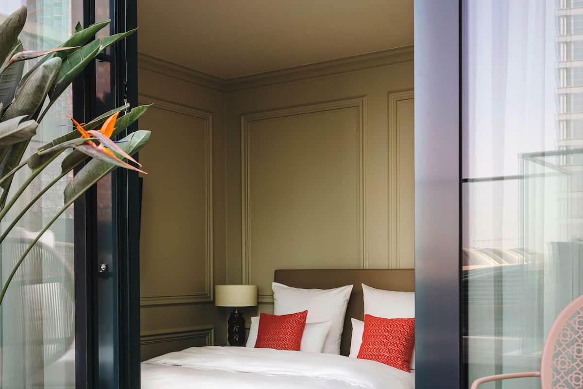 Ein Hotelzimmer mit Bett, Kissen, Lampe, Sessel und Pflanze.