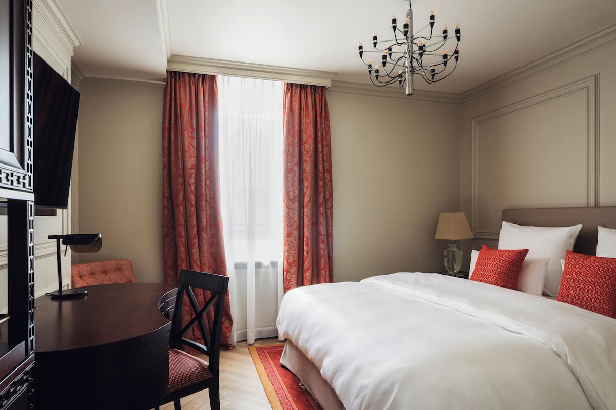 Ein Hotelzimmer mit Bett, Schreibtisch, Stuhl, Fernseher und einer Chandelier.
