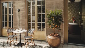 An outdoor seating area with two checkered chairs, a round table, and a large planter with an orange tree.