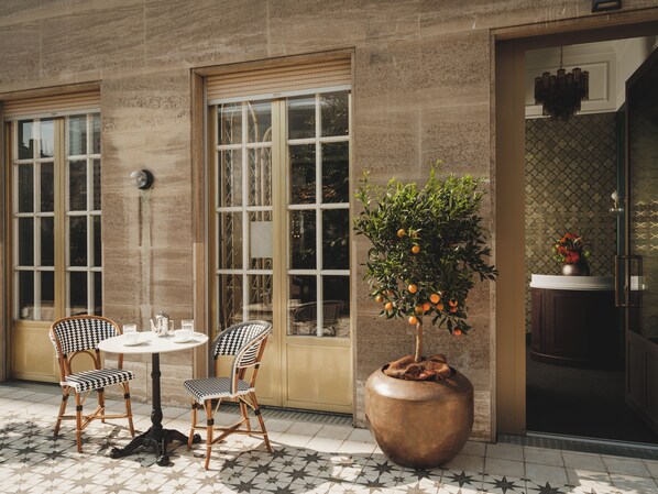 An outdoor seating area with two checkered chairs, a round table, and a large planter with an orange tree.