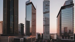 A cityscape with modern high-rise buildings, including a prominent glass skyscraper with a unique angular design.