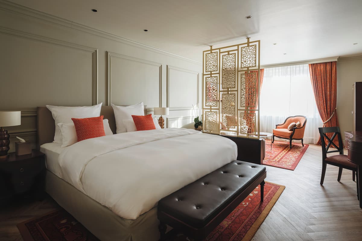 Ein geräumiges Hotelzimmer mit einem großen Bett, einer Bank, einem Sessel und einem dekorativen Raumteiler.