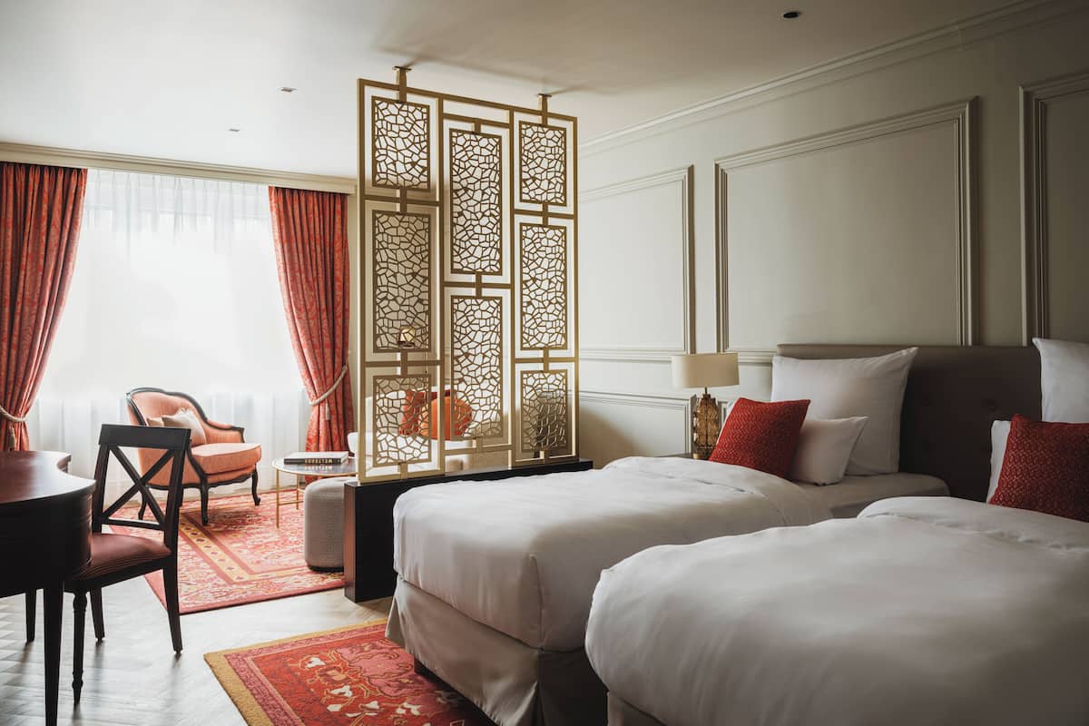 Ein Hotelzimmer mit zwei Betten, einem Schreibtisch, einem Stuhl, einem Dekosparren und Blick ins Freie.