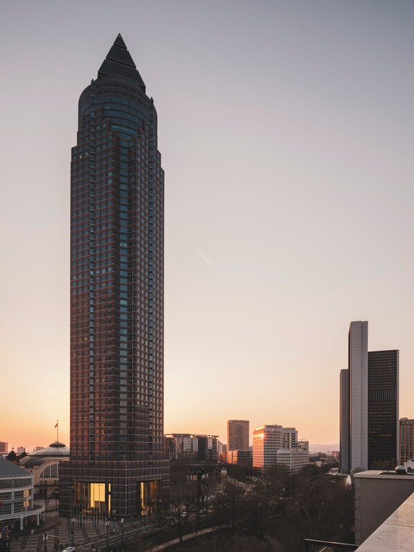 Un rascacielos alto y moderno con una punta distintiva, rodeado de otros edificios y un cielo despejado.