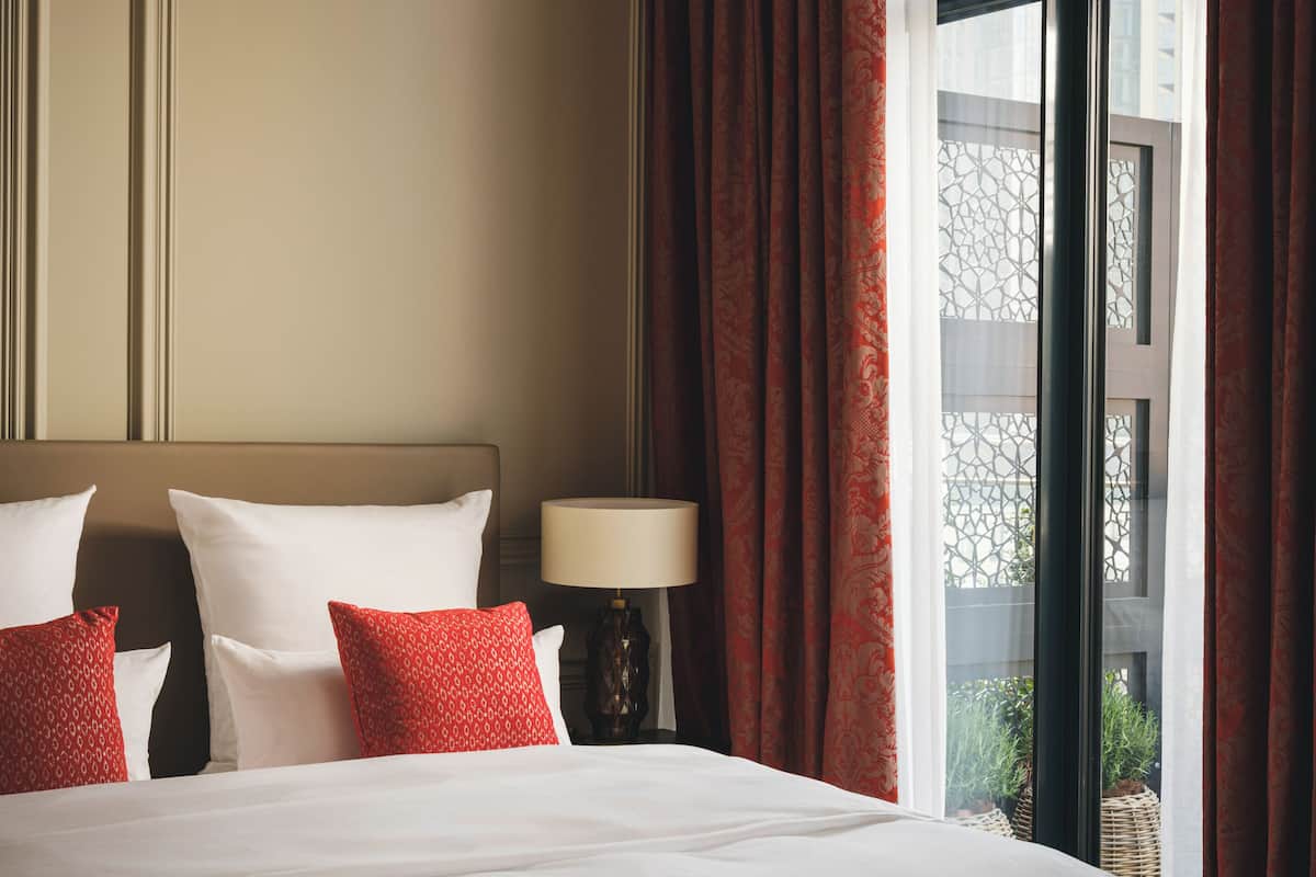 Ein Hotelzimmer mit einem großen Bett, einem Nachttisch mit Lampe und einem Fenster mit Vorhängen.