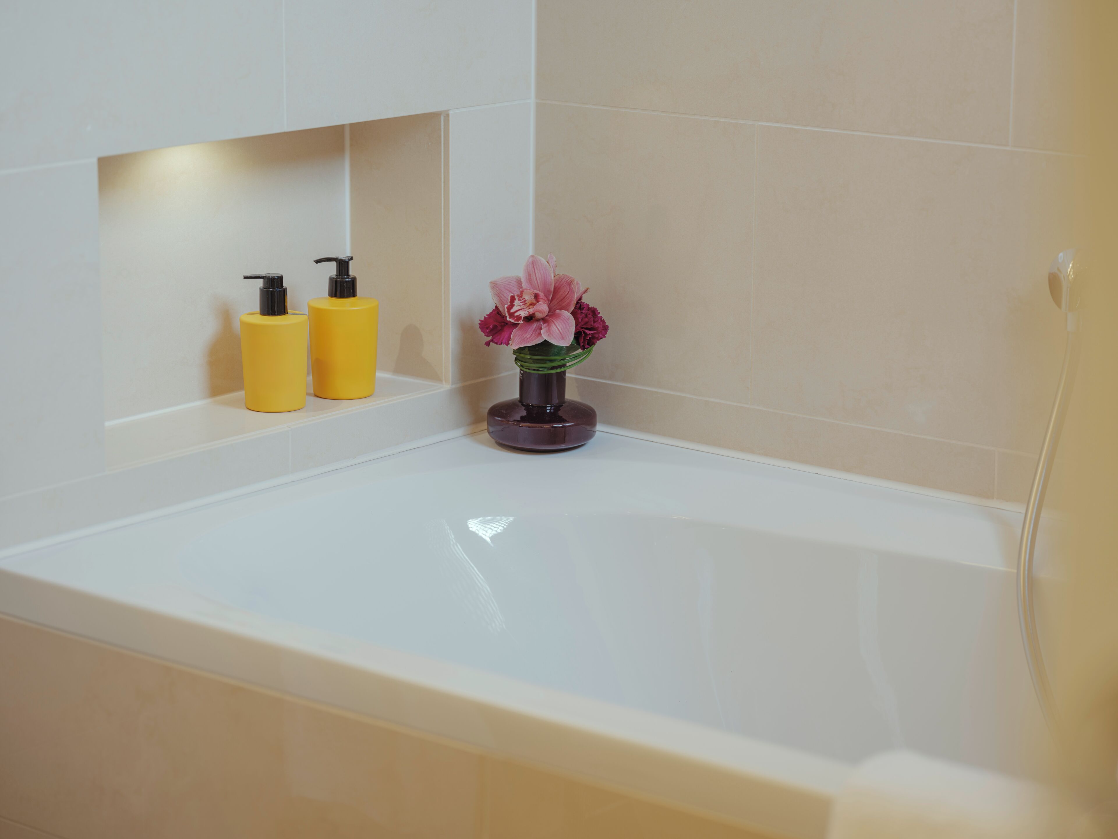 A bathroom with a bathtub, two yellow bottles, and a vase with pink flowers.