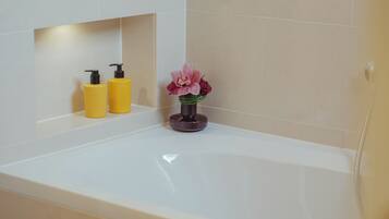 A bathroom with a bathtub, two yellow bottles, and a vase with pink flowers.