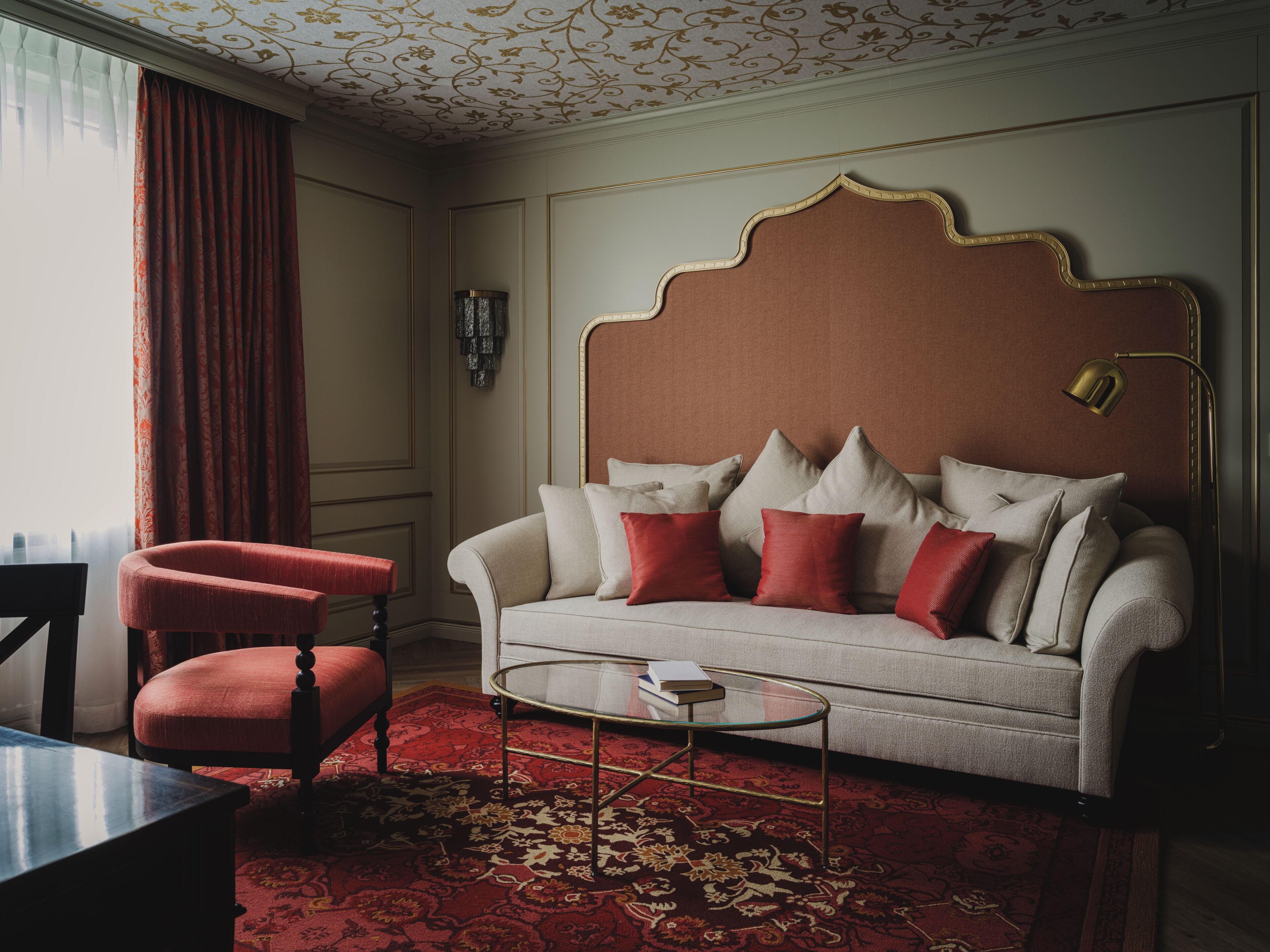 A room with a sofa, a red chair, a coffee table, and a patterned carpet.
