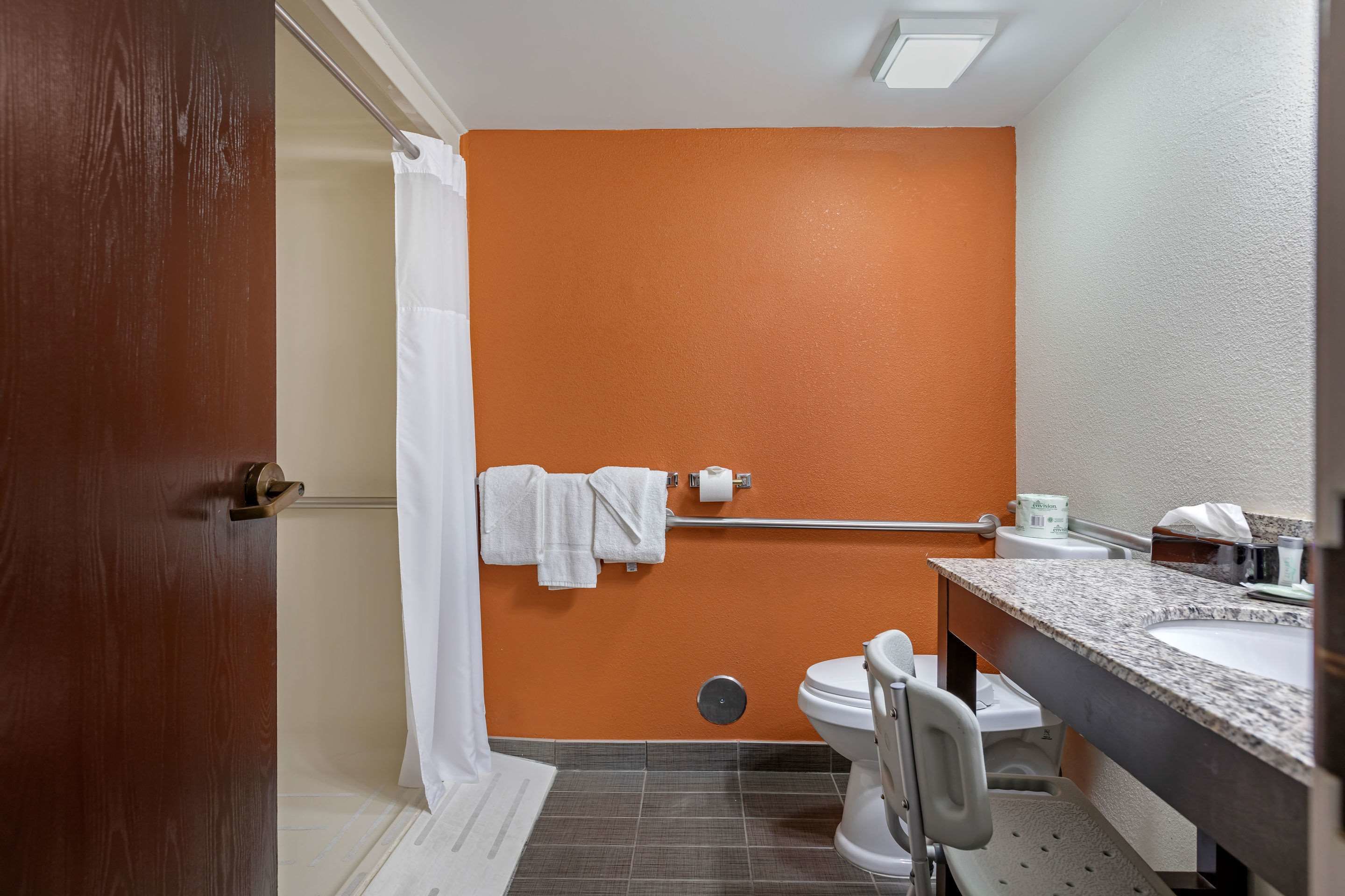Une salle de bain avec un mur orange, des toilettes blanches, un lavabo avec un plan de travail en granit et un rideau de douche.