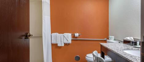 Une salle de bain avec un mur orange, des toilettes blanches, un lavabo avec un plan de travail en granit et un rideau de douche.