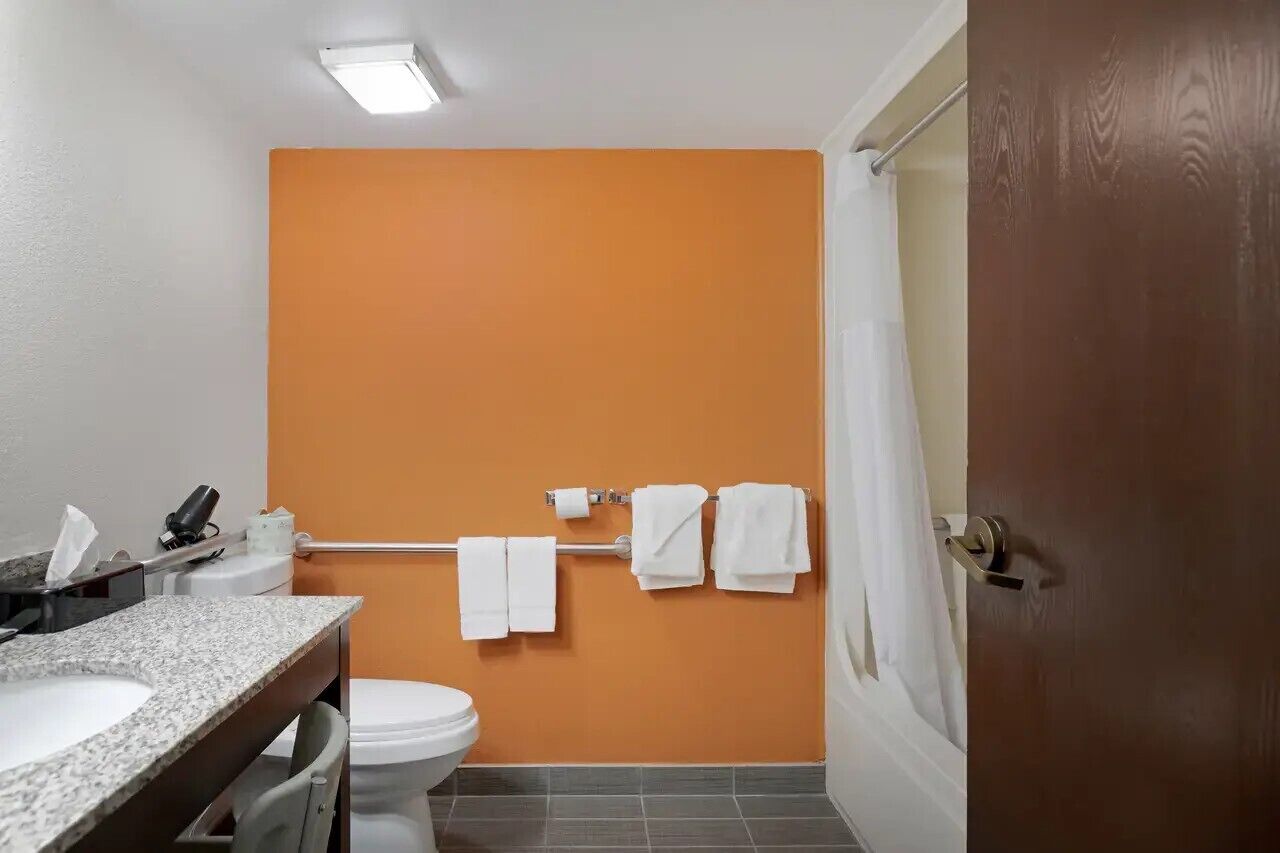 Un baño con una pared naranja, un inodoro blanco, un lavabo con encimera de granito y un perchero con toallas blancas.
