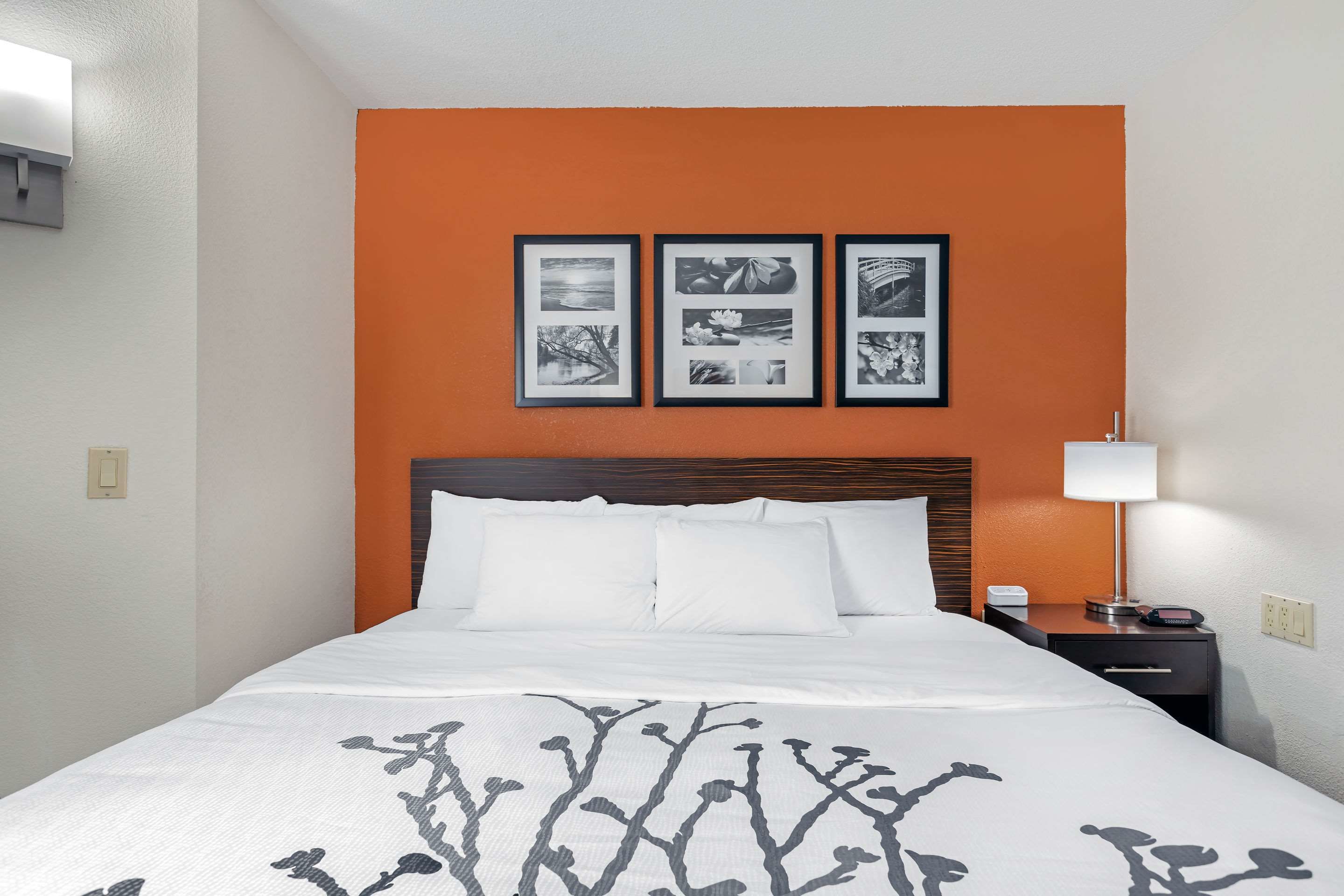 A hotel room with a bed, a nightstand, a lamp, and three framed pictures on the wall.