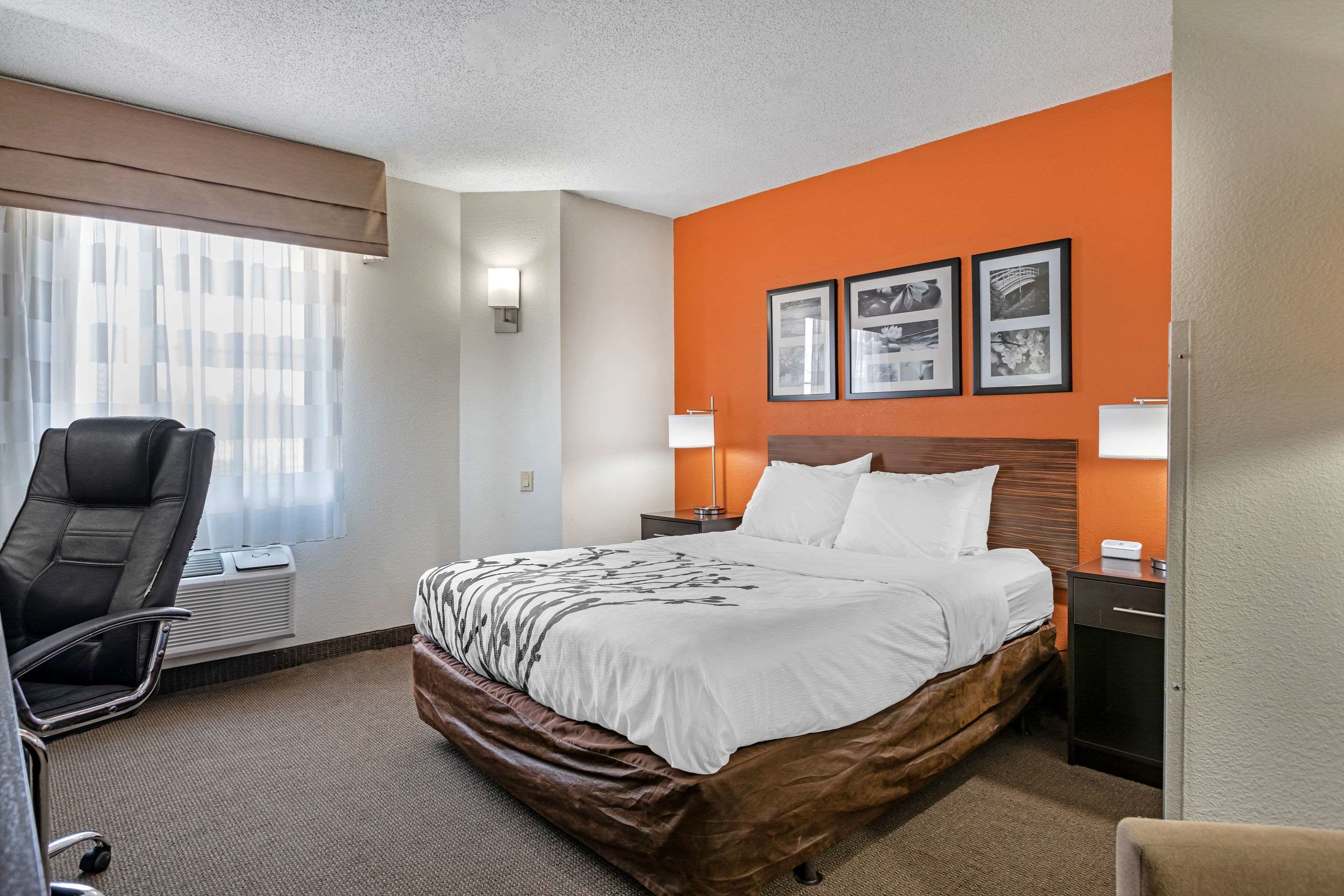 Una habitación de hotel con una cama grande, un escritorio, una silla y un ventanal con cortinas.