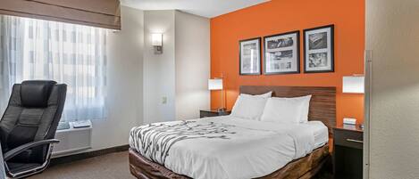 A hotel room with a large bed, a desk, a chair, and a window with curtains.