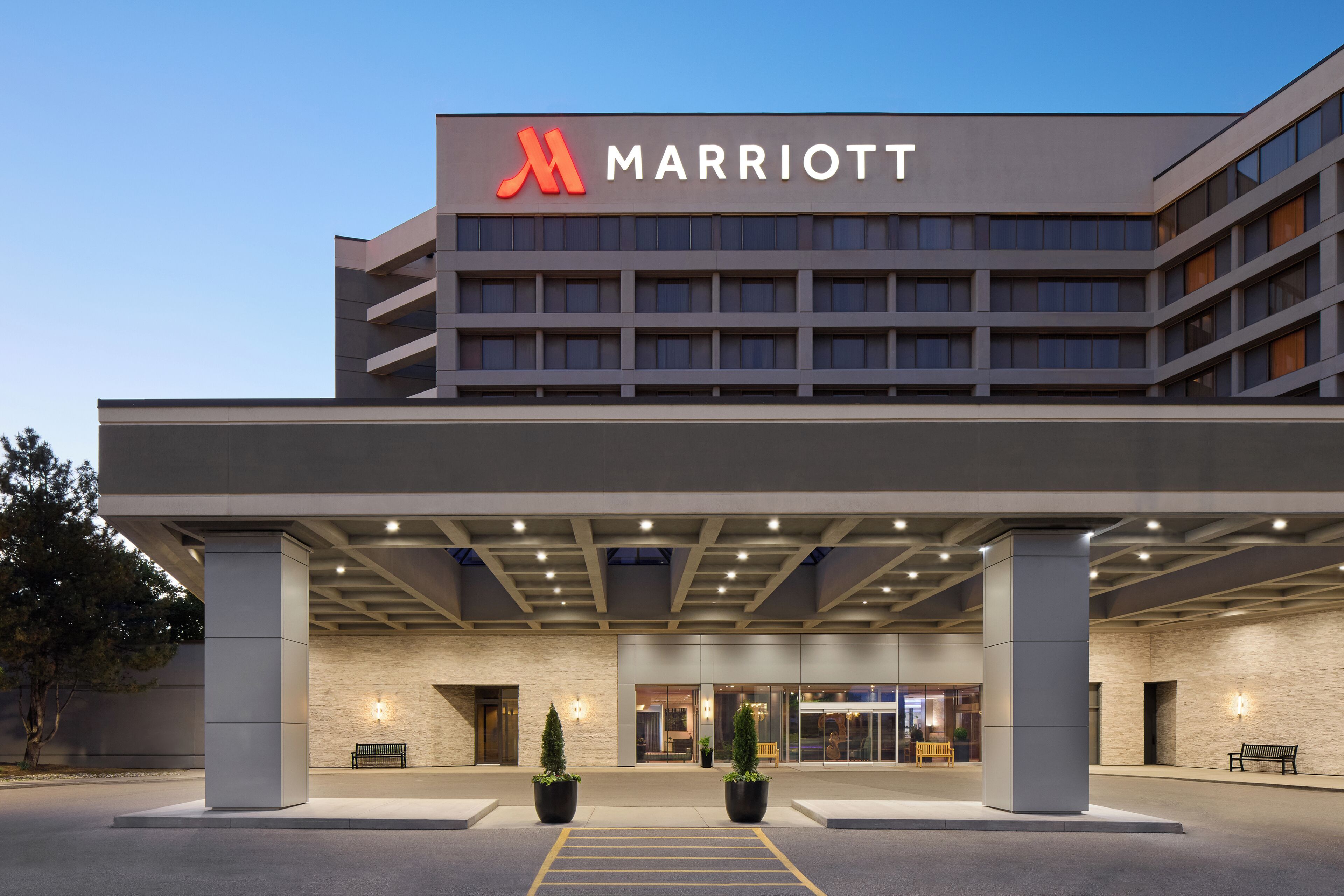 A Marriott hotel entrance with a covered walkway, large potted plants, and a clear sky.