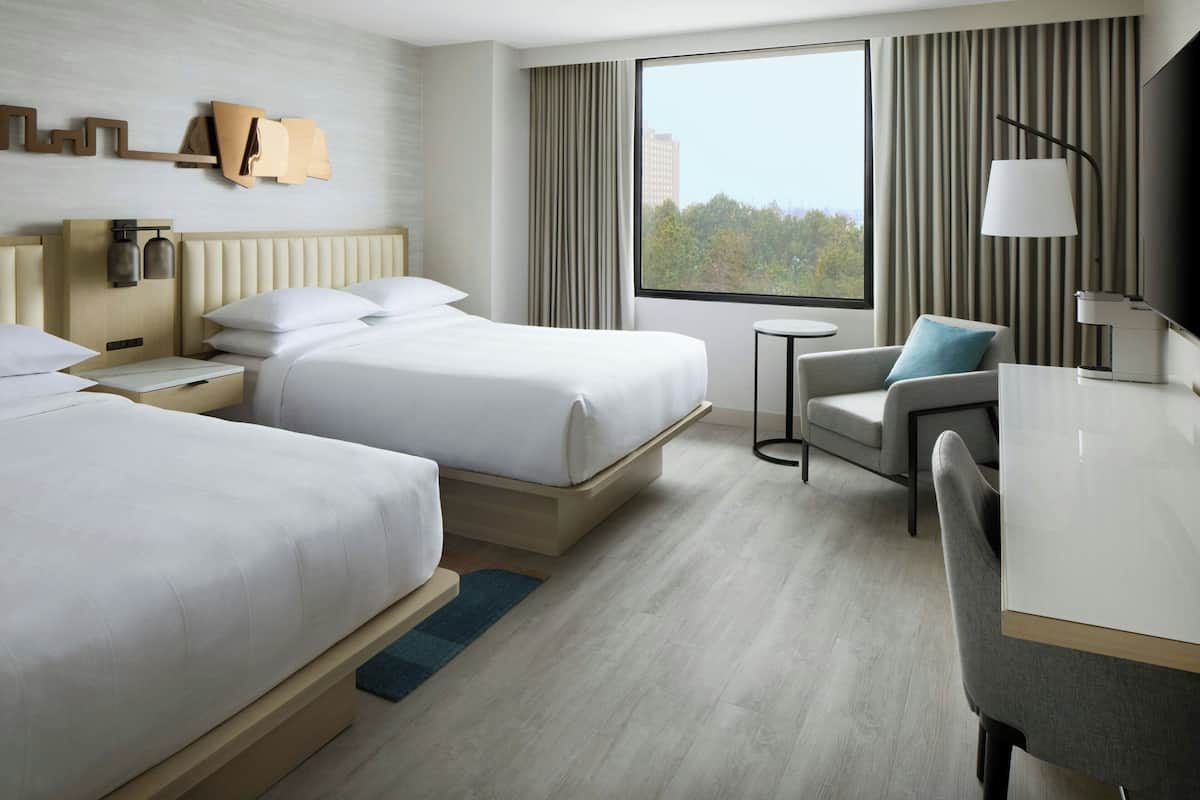 A hotel room with two beds, a desk, a chair, a TV, and a window with curtains.
