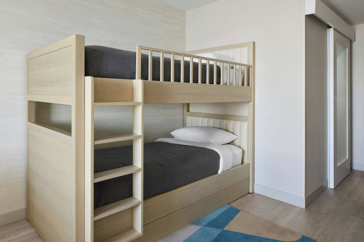 Una cama litera con estructura de madera, un estante inferior y un colchón con almohadas.