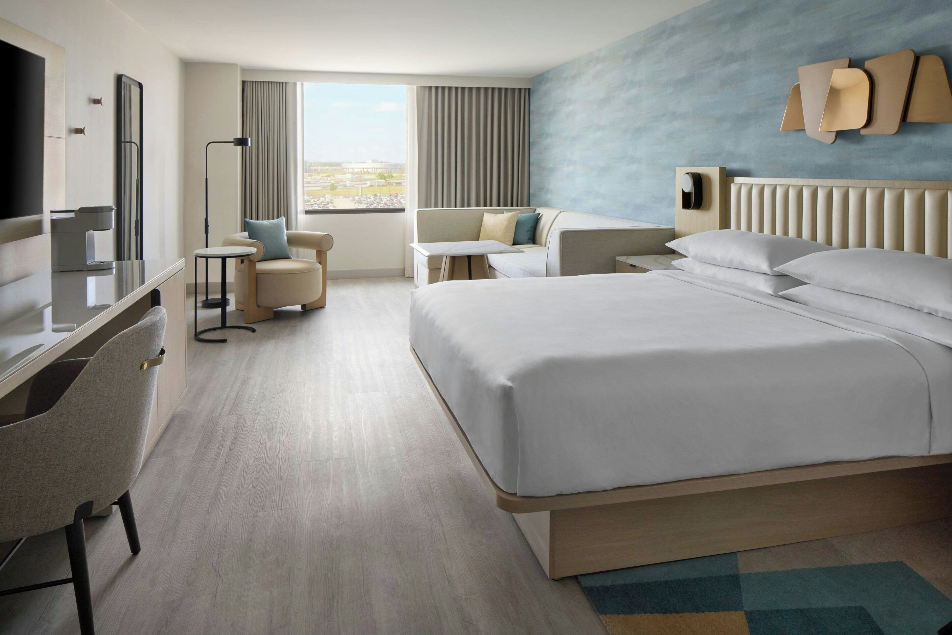 A modern hotel room with a large bed, a desk, a chair, a TV, and a window with curtains.