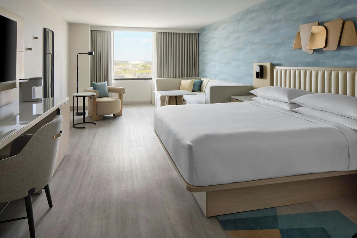 A modern hotel room with a large bed, a desk, a chair, a TV, and a window with curtains.