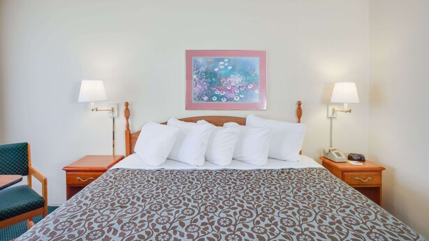 A hotel room with a bed, two bedside tables, a chair, and a painting on the wall. - Days Inn by Wyndham Newport (Newport)
