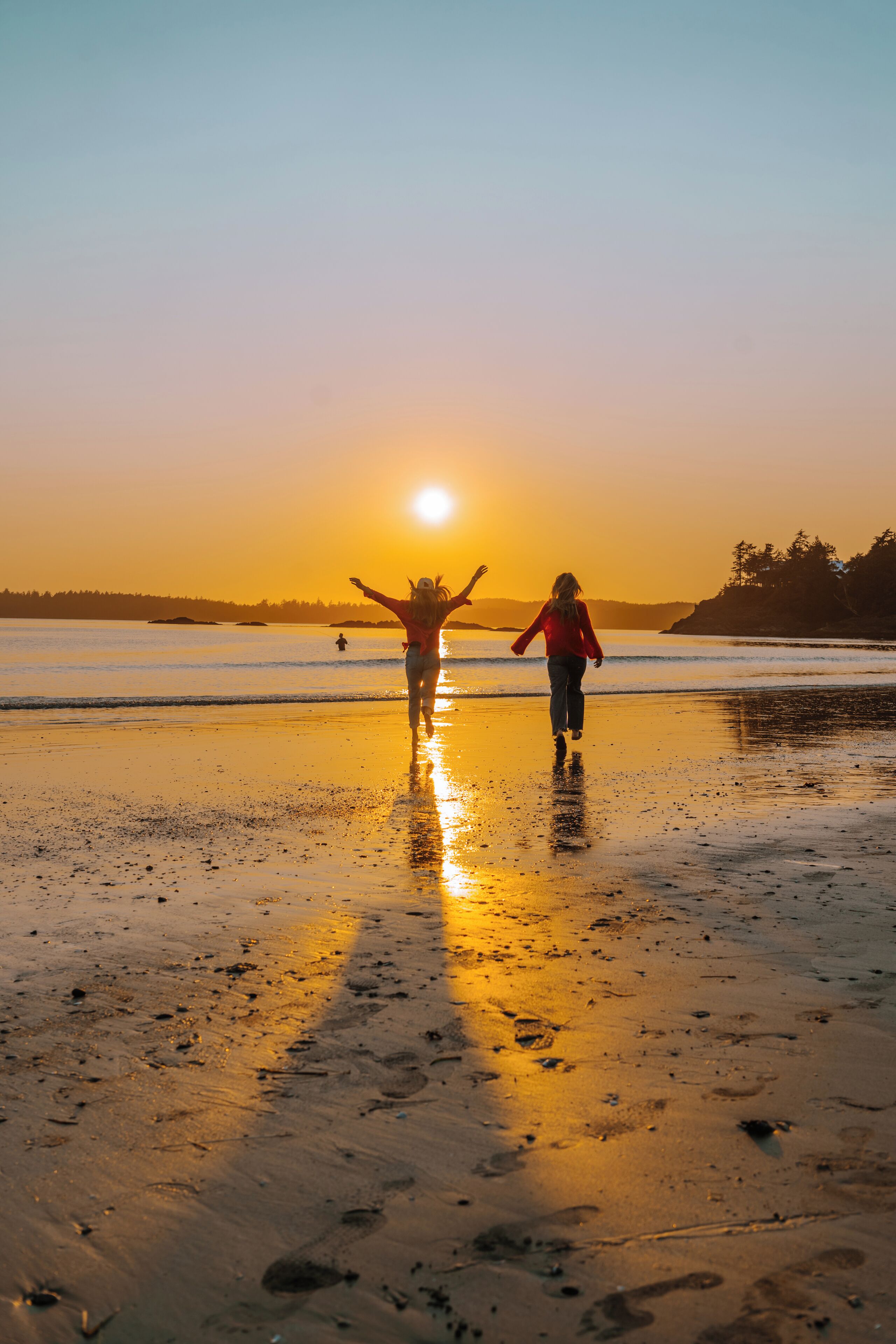 A beach scene with two people walking towards the sunset.
