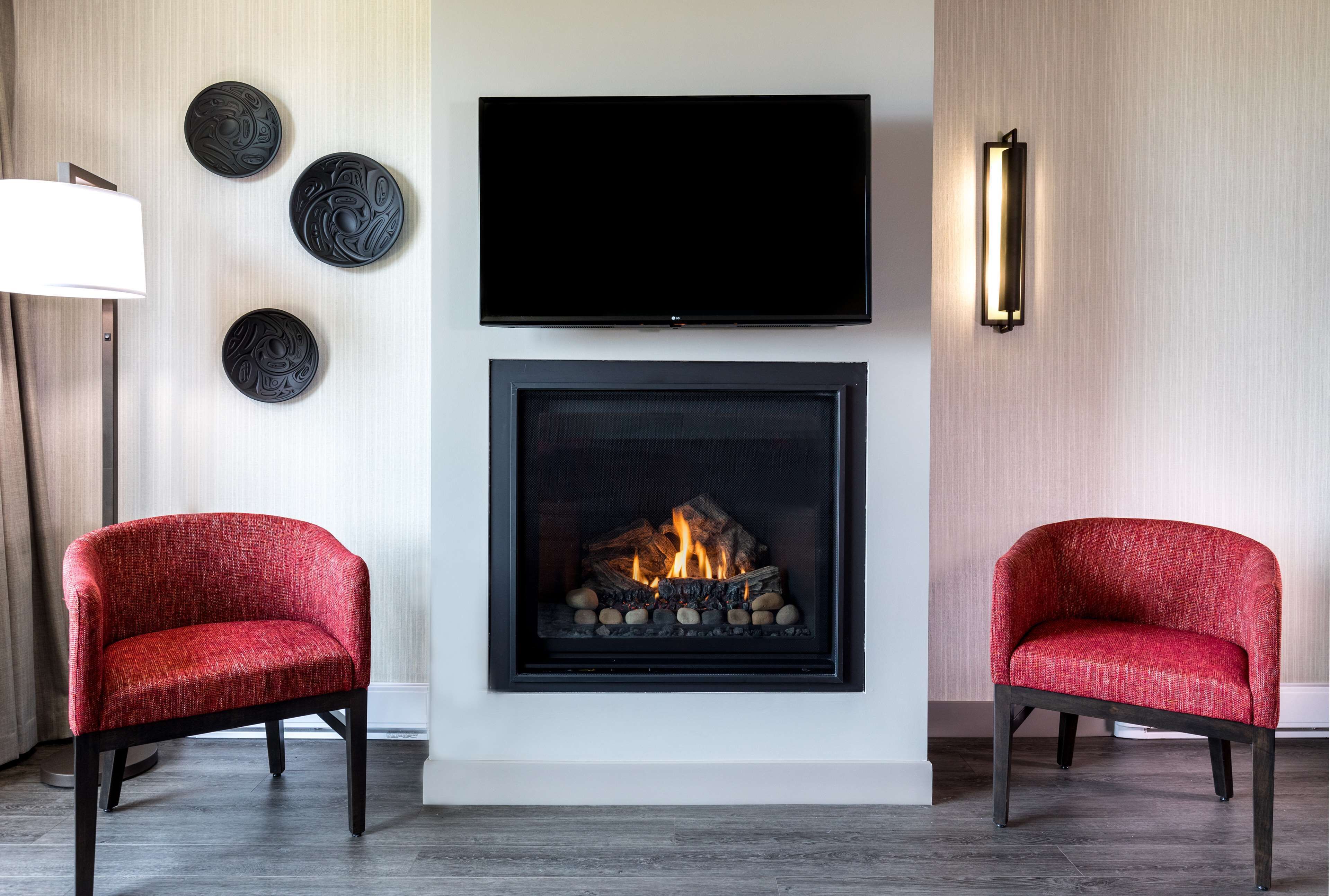 Uma sala de estar moderna com lareira, duas poltronas vermelhas, uma TV de tela plana e pratos decorativos na parede.