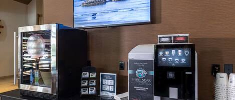 A coffee station with a coffee machine, a refrigerated display case, and a television mounted on the wall.