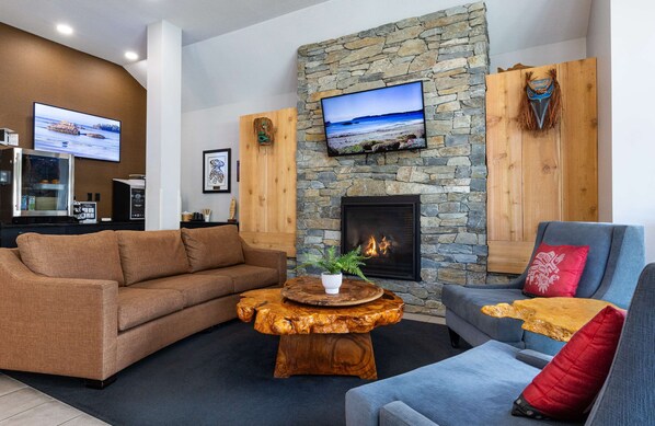 A cozy living room with a stone fireplace, a television mounted on the wall, and a wooden coffee table. - Best Western Plus Tin Wis Resort (Tofino)