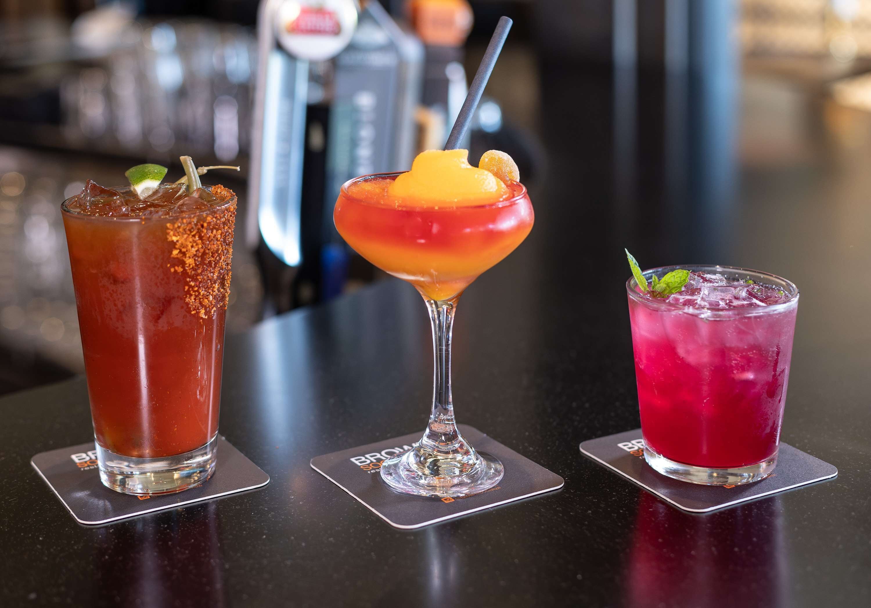 Three cocktails on a bar counter with a blurred background.