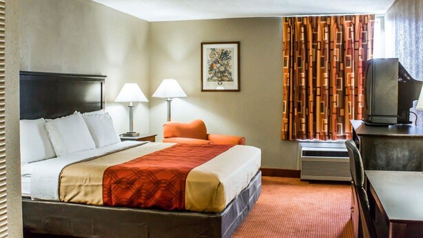 A hotel room with a bed, two bedside lamps, a television, and a framed picture on the wall.