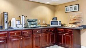 A kitchen with a coffee station, microwave, and a display case with pastries.