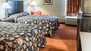 A hotel room with two beds, a desk with a lamp, a television, and a framed floral artwork on the wall.