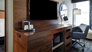 A hotel room with a wooden desk, a flat-screen TV, a mirror, a lamp, and a chair. - Hampton Inn I-75 Lexington/Hamburg Area (Lexington)
