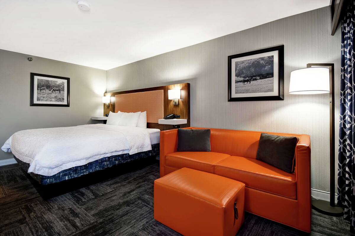 A hotel room with a bed, a sofa, a nightstand, and two wall-mounted lamps.