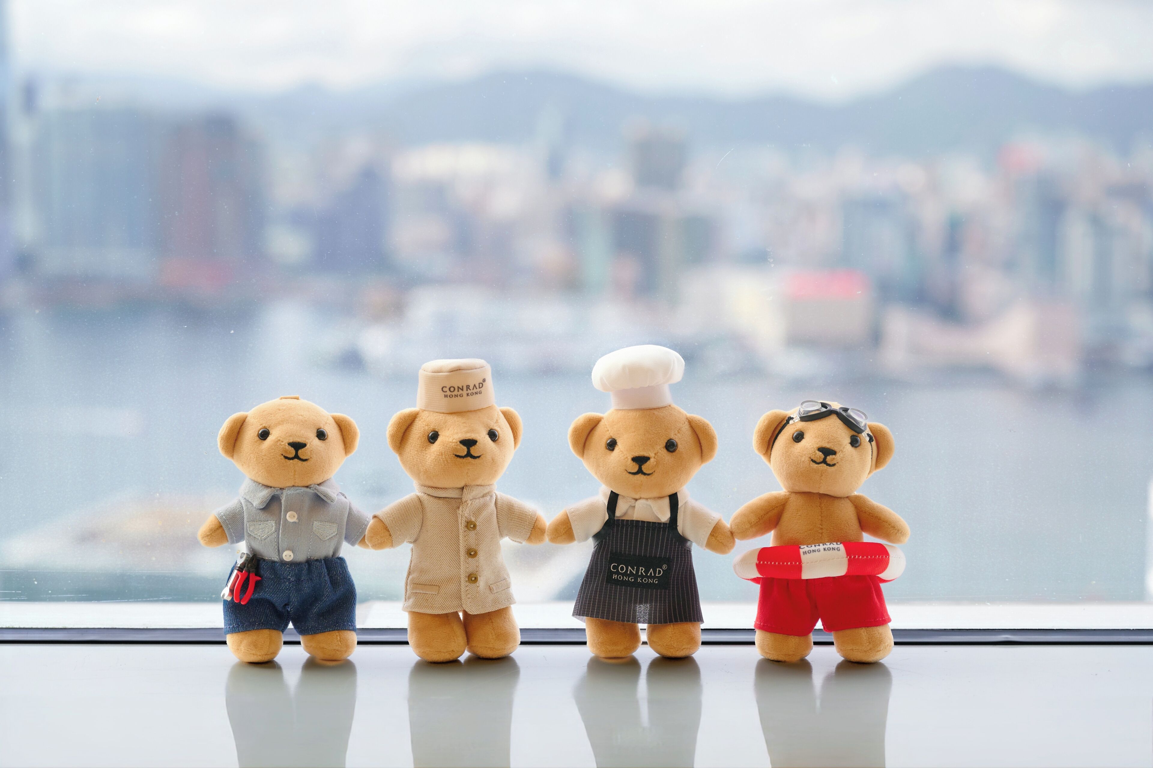 Four teddy bears on a windowsill with a cityscape view.