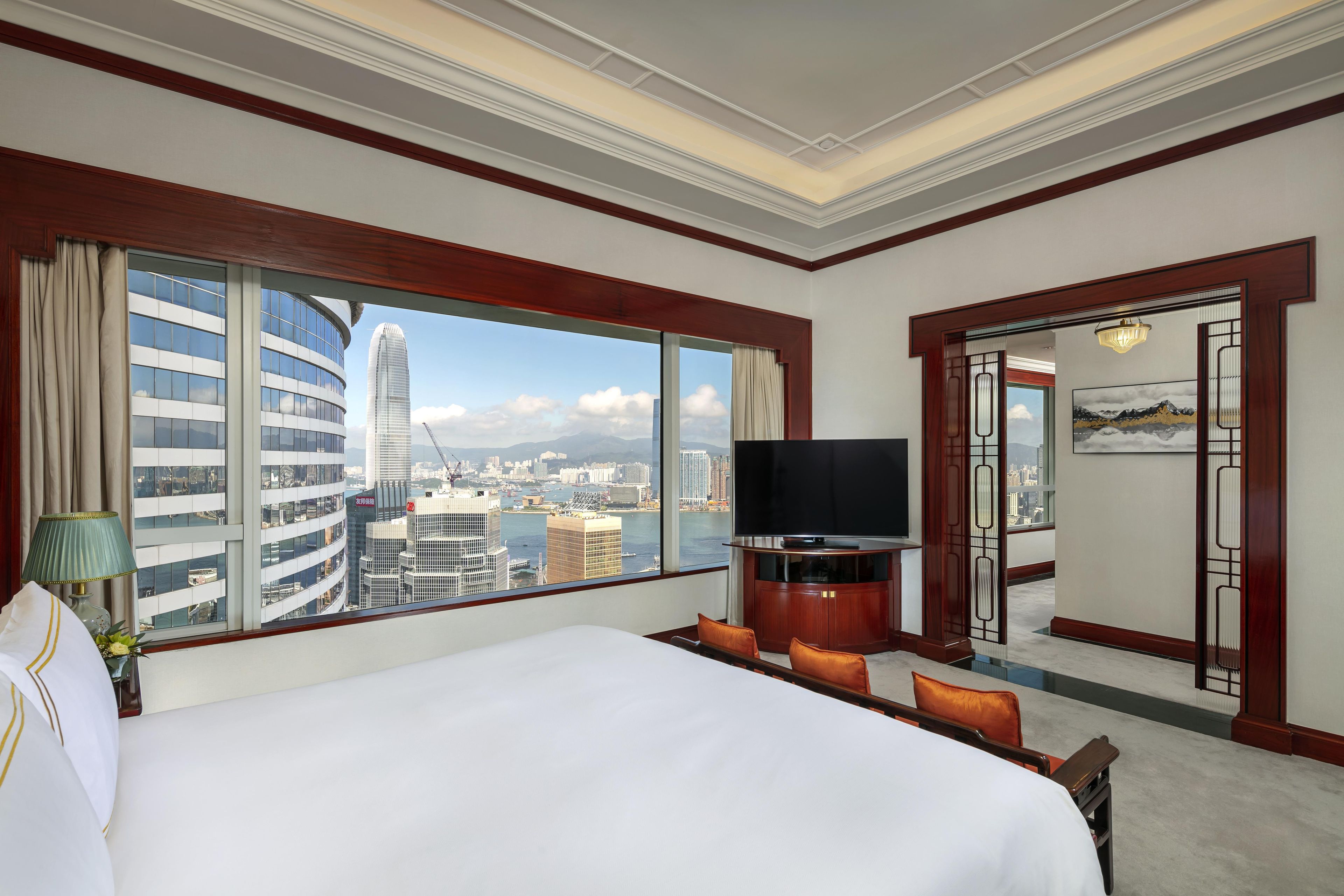 Habitació d'hotel amb un llit gran, televisió i vista a un paisatge urbà a través d'una finestra ampla.