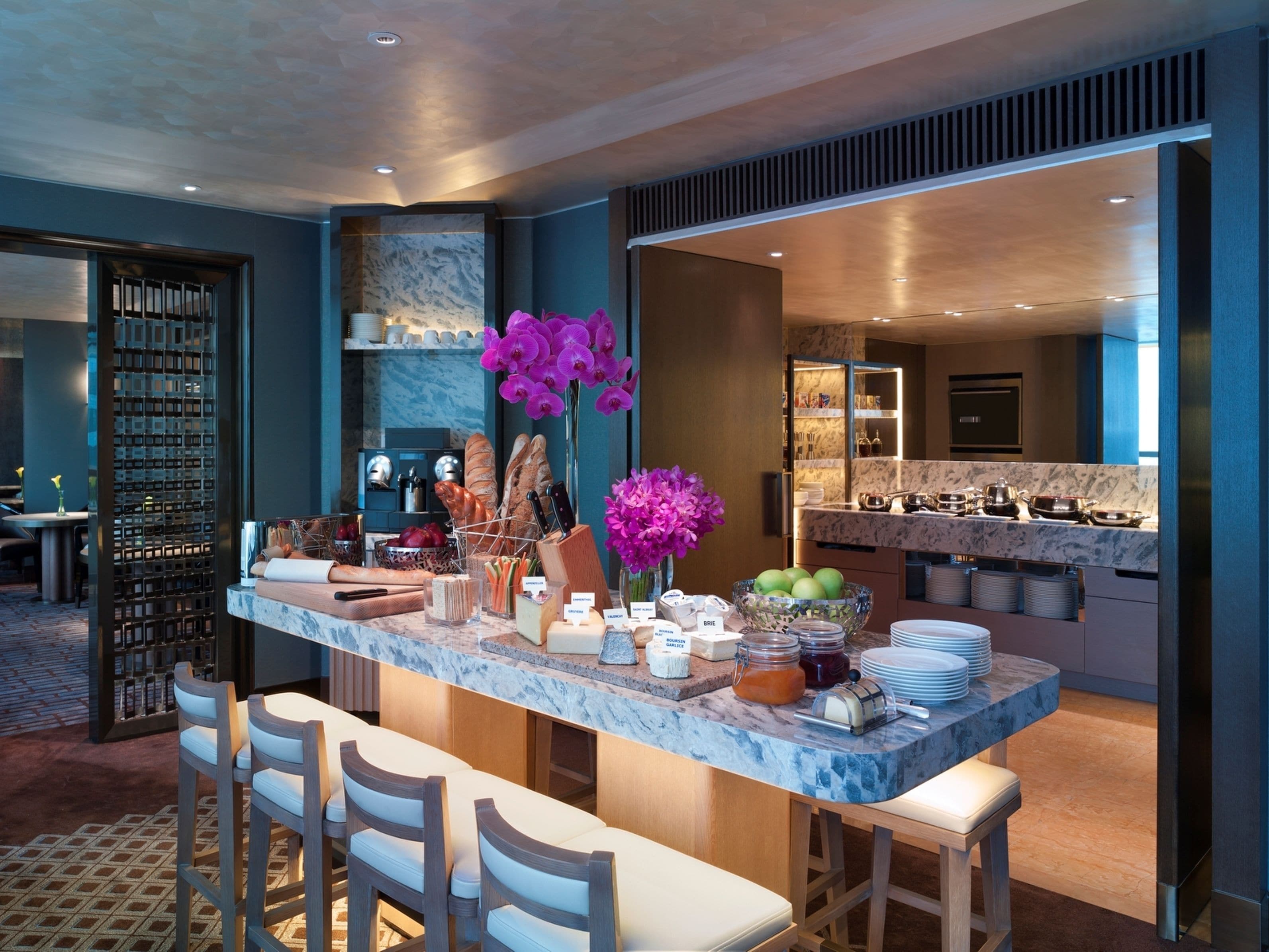 A modern kitchen with marble countertops, a central island with bar seating, and a view into the dining area.