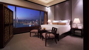A hotel room with a large bed, two bedside tables, a desk, and a view of a cityscape at dusk. - Conrad Hong Kong (Hong Kong)