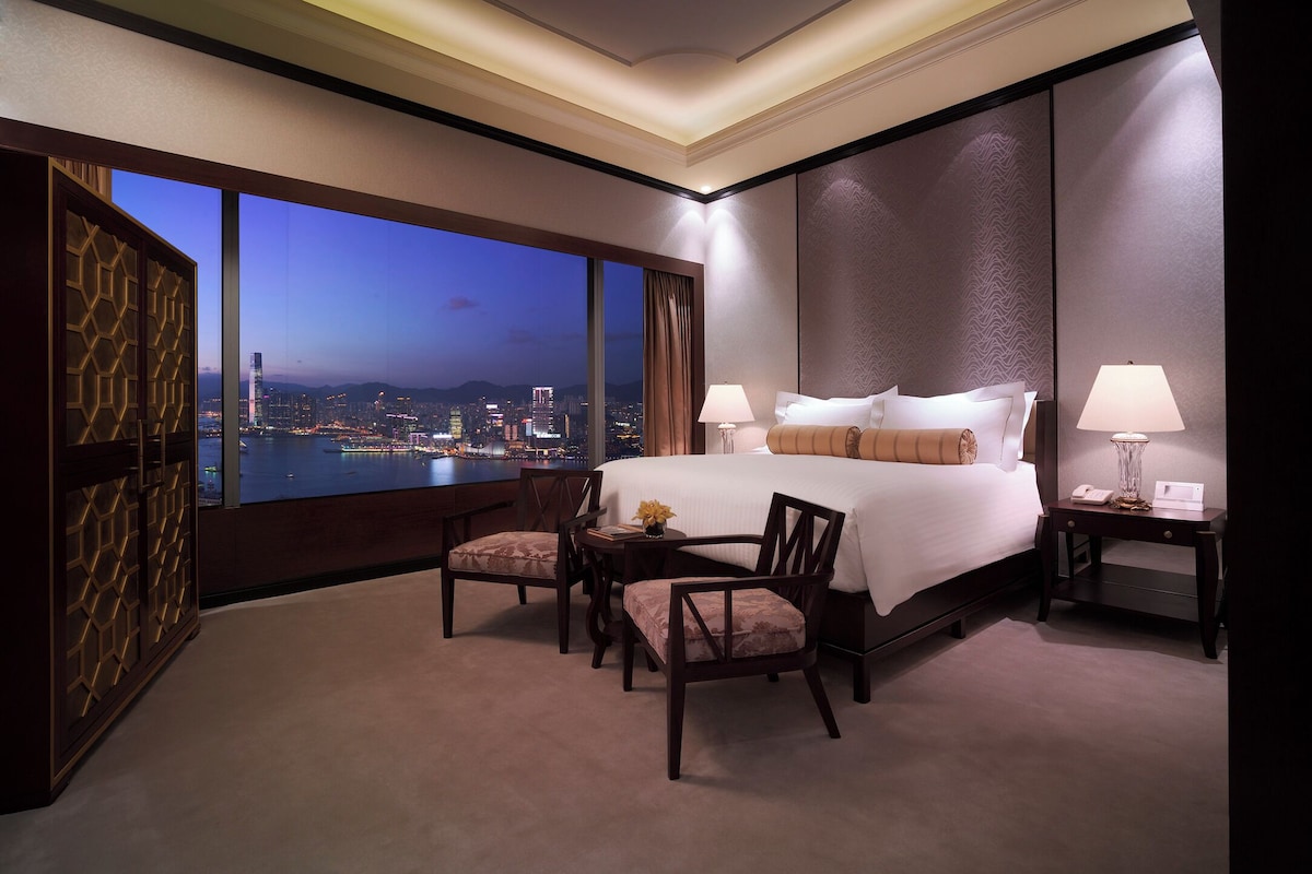 Camera d'albergo con un letto grande, due comodini, una scrivania e vista sulla città al crepuscolo.