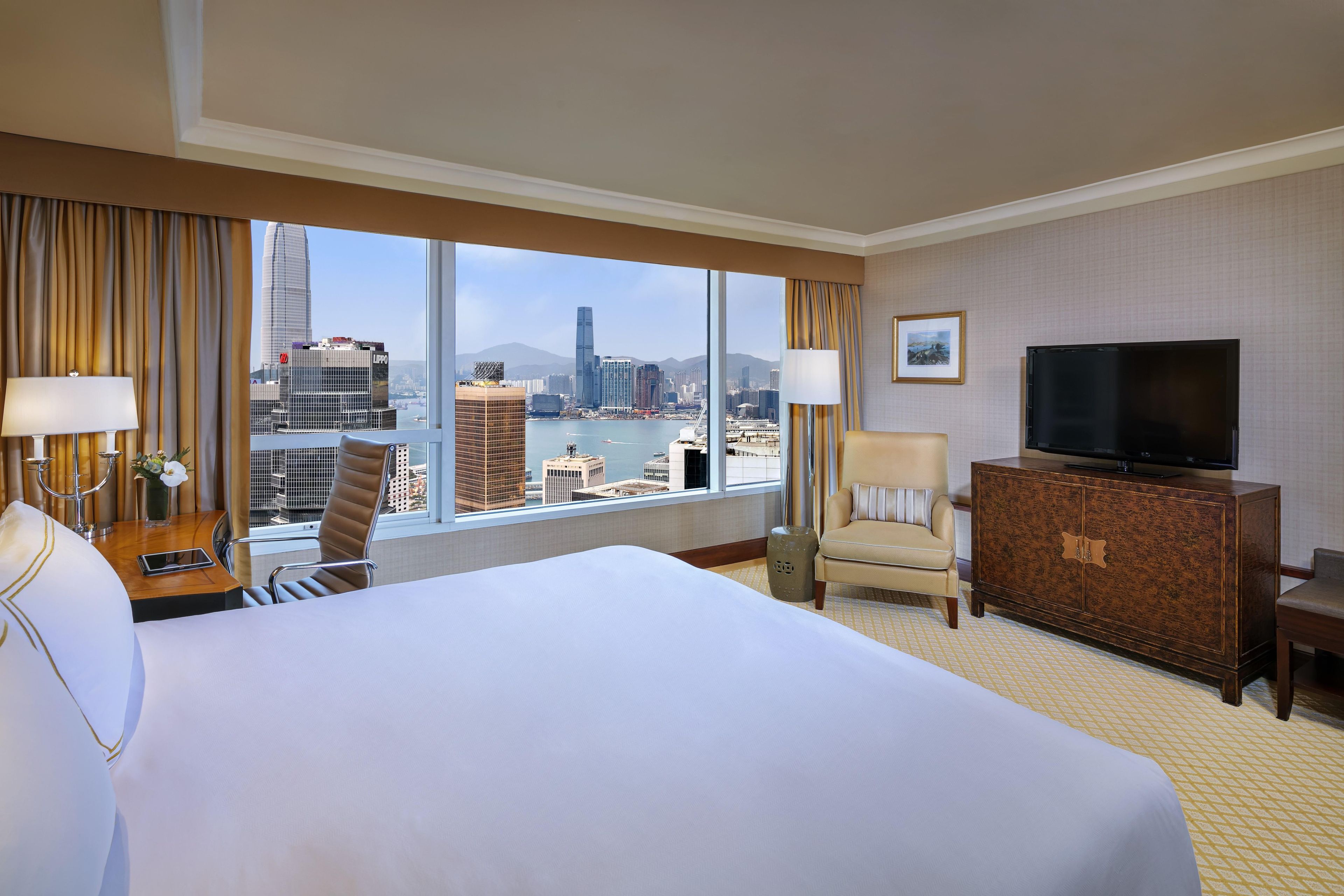 Une chambre d’hôtel avec un grand lit, une télévision, un bureau avec une lampe, une chaise et une vue sur le paysage urbain.
