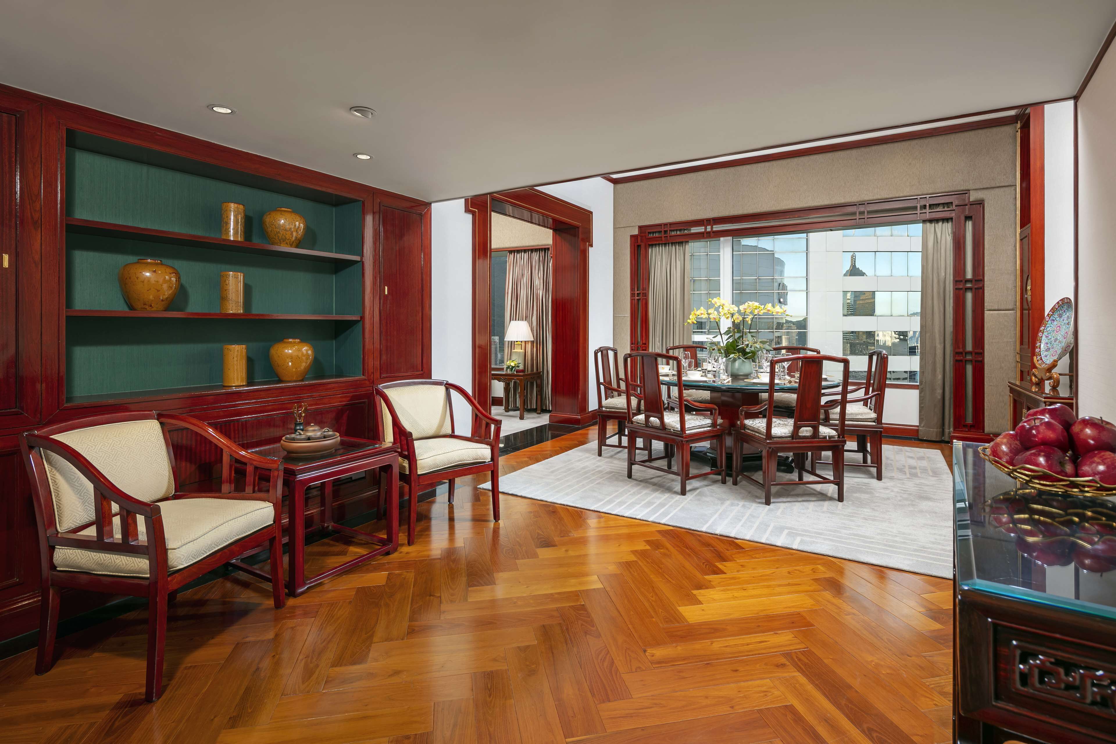 A dining area with wooden furniture, a glass table, and a view of the city through large windows.