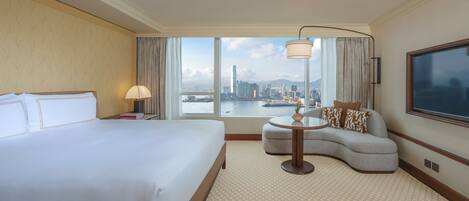 A hotel room with a large bed, a sofa, a small table, and a TV. There is a window with a city view.