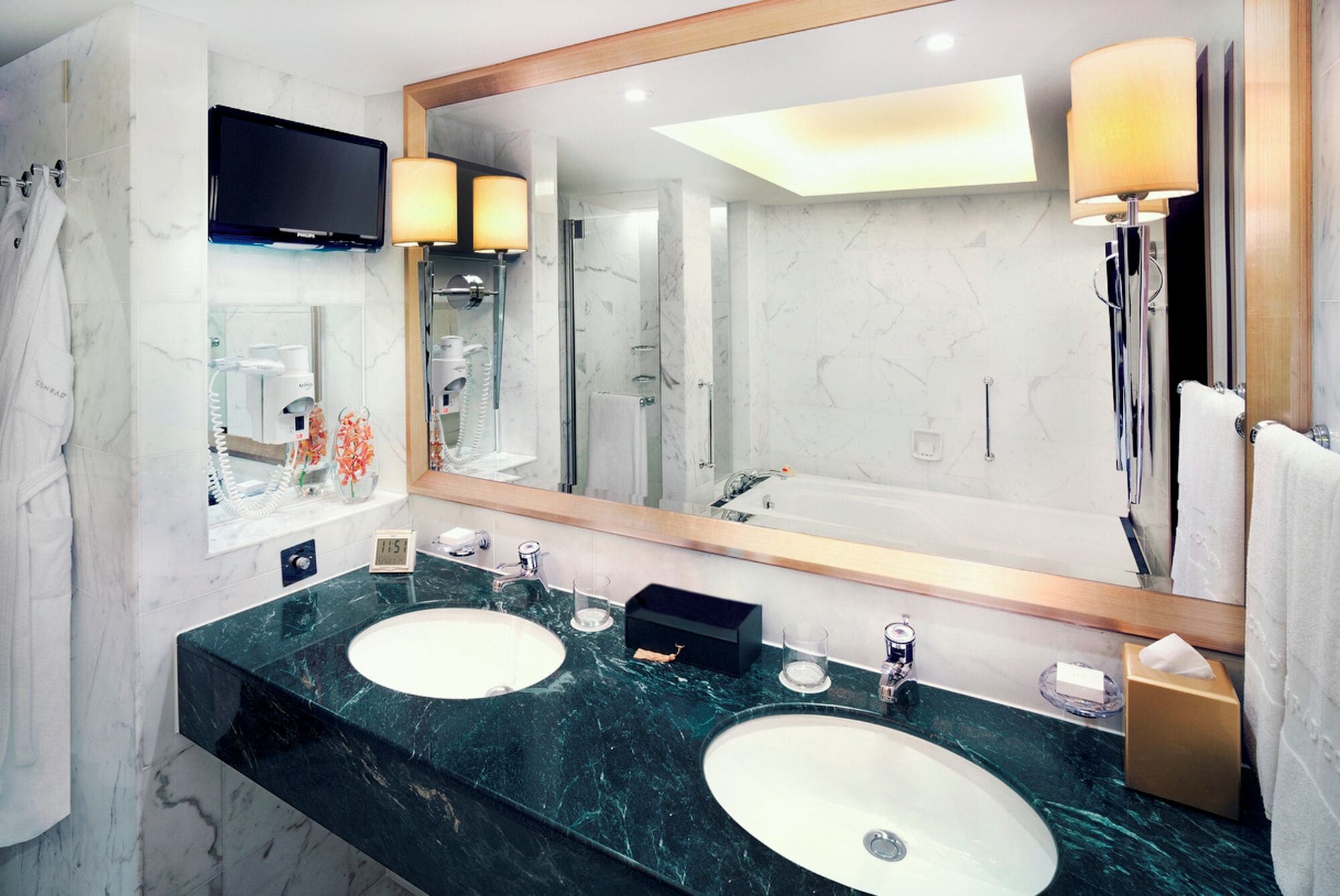 A modern bathroom with two sinks, a large mirror, a TV, and a shower.